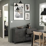 Modern kitchen with black and light wood furniture. Gray cabinets, hanging lamps, and printed art on green walls.