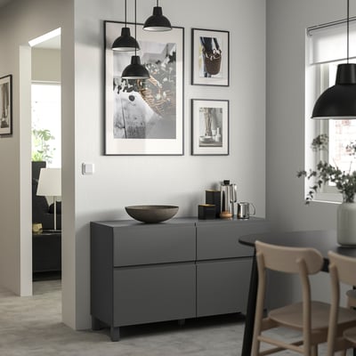 Modern living space with grey BESTÅ storage unit, featuring pendant lights, framed art, and wooden chairs.