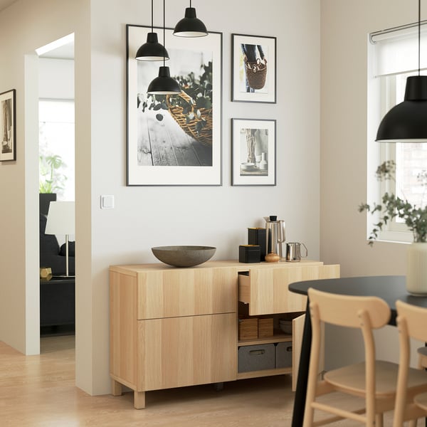 Modern dining area with wooden sideboard, black lamps, chairs, and wall art. Minimalistic and well-lit.