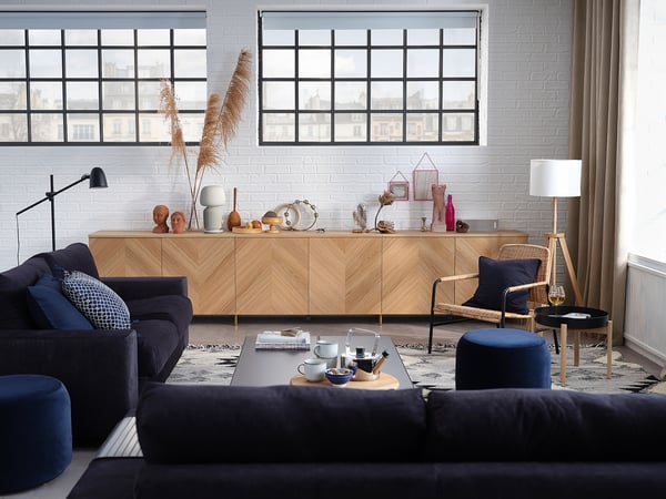 Contemporary living room with navy blue sofa, wooden sideboard, potted plants, and large windows.