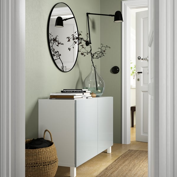 Modern hallway with BESTÅ sideboard, books, vase, mirror, basket, lamp; leads to another room.