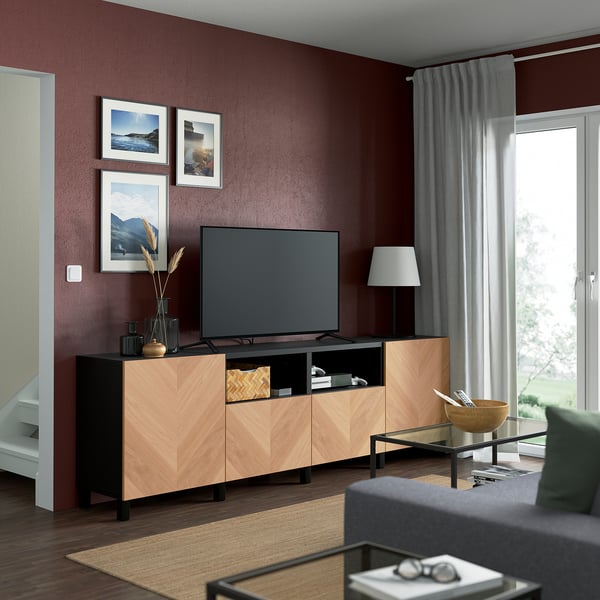 Modern living room with maroon walls, BESTÅ tv bench, flat screen tv, photos, lamp, coffee table, and grey curtains.