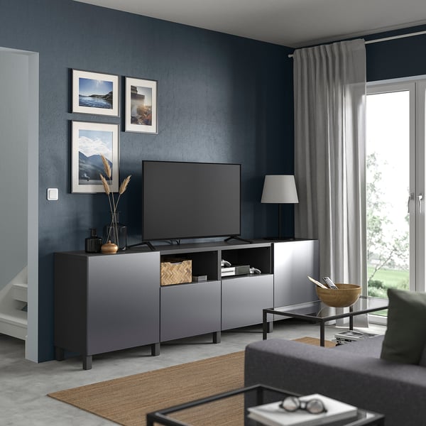 Modern living room with dark blue walls, grey BESTÅ tv bench, flat screen tv, stylish decor, and large window with grey curtains.
