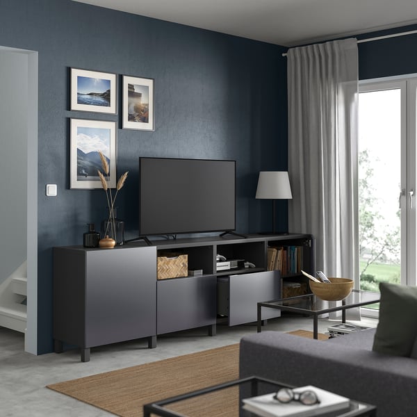 Modern living room with BESTÅ tv cabinet and grey curtains, flat-screen tv, pictures, lamp, and a sofa with a wooden bowl.