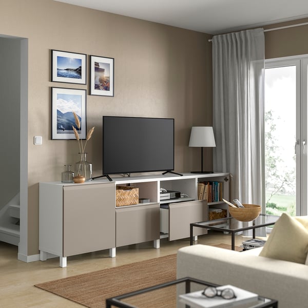 White BESTÅ tv bench in living room. Tv, decor, books. Large window with curtains. Beige sofa by wooden coffee table.