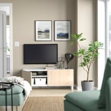Modern living room with light beige BESTÅ tv unit, green cushioned chairs, a potted plant, and framed nature photos.