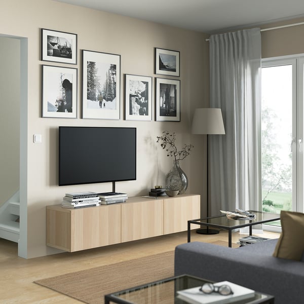 Modern living room with BESTÅ tv bench in light oak, featuring storage shelves, art above, and a silver vase to the side.