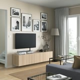 Modern living room with BESTÅ tv bench in light oak, featuring storage shelves, art above, and a silver vase to the side.