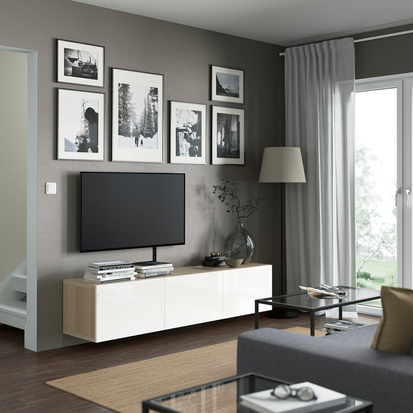 Modern living room with large tv mounted on a white BESTÅ tv bench. The bench has black frames, a glass coffee table, and black sofa.