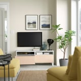Modern living room with BESTÅ tv unit, flat-screen tv, framed photos, large houseplant, yellow chairs, and natural decor.