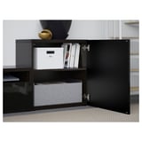 Black BESTÅ cabinet with open door revealing storage: white boxes, books, gray drawer.