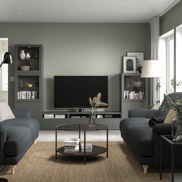 Contemporary living room with BESTÅ tv bench, flat-screen tv, grey sofas, glass coffee table, sage green walls.
