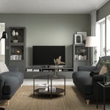 Contemporary living room with BESTÅ tv bench, flat-screen tv, grey sofas, glass coffee table, sage green walls.