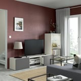Modern living room with maroon walls, BESTÅ tv unit, flat-screen tv, lamp, glass coffee table with magazines, and window with curtains.