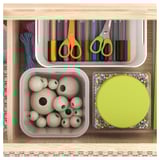 Organized storage shelf with crafts: colored pens, scissors, wooden beads, and a round container with beads.