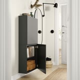 Modern hall: dark gray BESTÅ cabinet mounted on white wall, open showing books, wooden box; above, black wall lamp, decorative items.