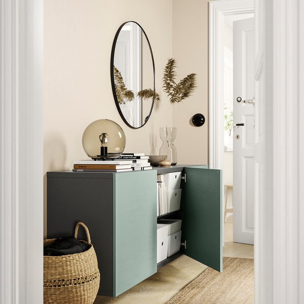Modern entryway with light blue BESTÅ storage unit, white walls, round mirror, and dried plants.