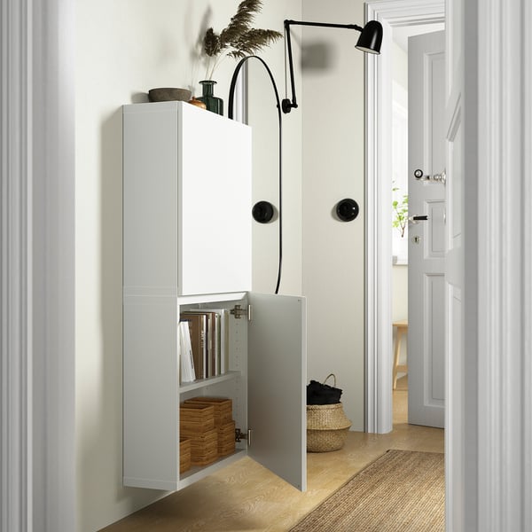 White wall-mounted cabinet, open doors showing books and boxes, black wall lamp above.