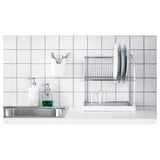 Kitchen sink with countertop, stainless steel, dish rack, green soap dispenser, white tiles.