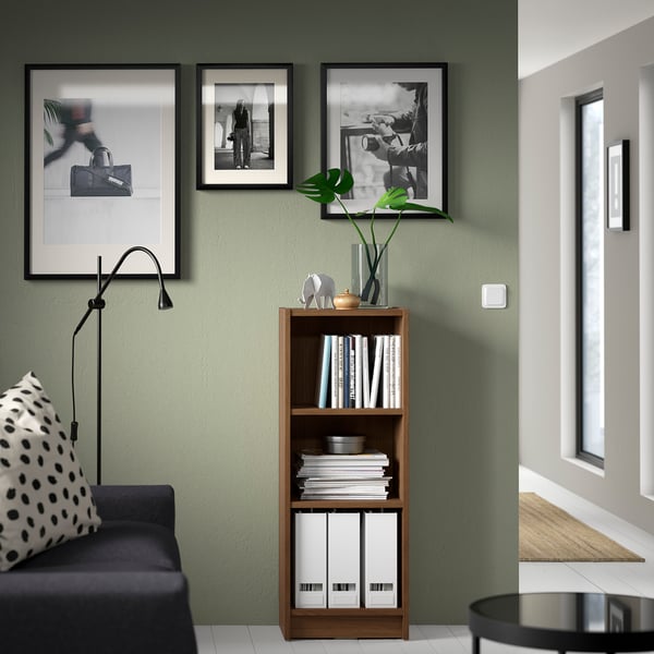 BILLY bookcase in modern living room, holding books & decor. Tall black lamp nearby. Black-and-white photos above.