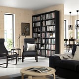 Room with large BILLY bookcase, armchair, coffee table, dining area, and pendant lamps.