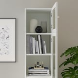 A white BILLY bookcase with glass doors books and decorative items. Adjustable shelves and hinges are visible, tailoring storage to needs.