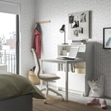 Home office with desk, laptop, chair, lamp, and clothes.