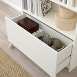 White BILLY bookcase drawer open, showing storage for decorations and box, with castors for smooth movement.