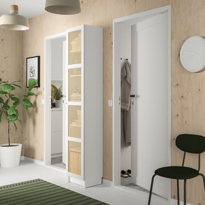Modern entryway with white BILLY bookcase, bamboo doors, black chair, plant, and coat hooks.