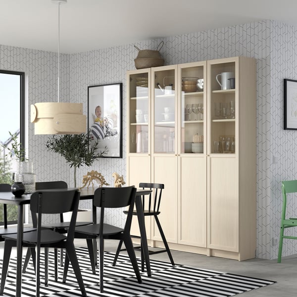 BILLY bookcase with glass doors in dining area, surrounded by chairs and rug, holding dishes and glassware, near pendant lamp.
