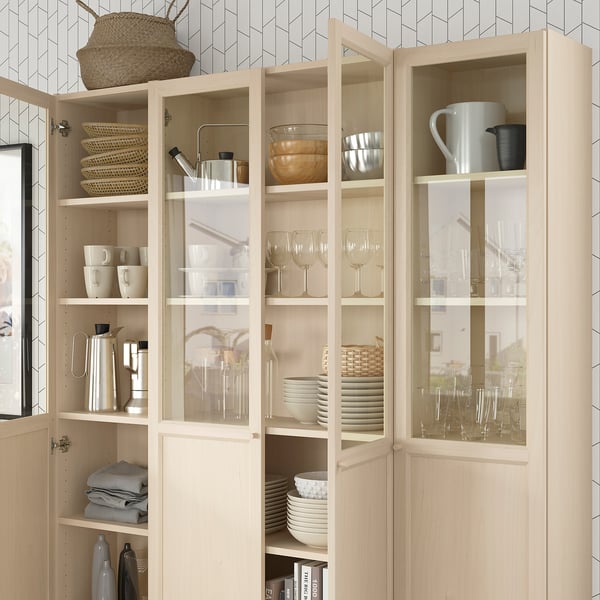 Wooden BILLY bookcase with glass doors, storing dishes, glasses, and is anchored to the wall.