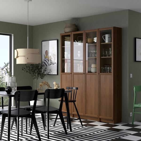Modern dining area with BILLY bookcase, dishware, black table, striped rug, and pendant light. Dark green wall with photograph.