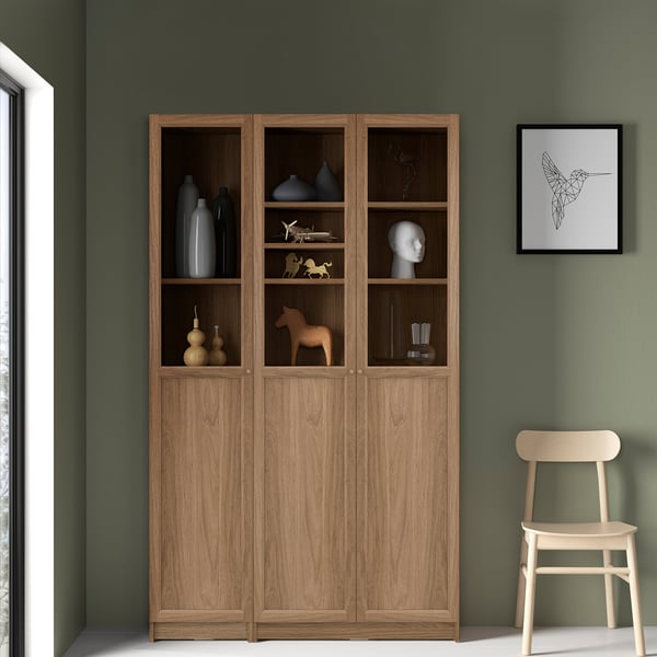 Large wooden BILLY bookcase against green wall, showcasing vases and figurines. Right side chair and wall art visible.