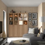 Living room with large wooden BILLY bookcase filled with books & decor. Grey sofa, coffee table, and hanging framed photos. Guitar on wall.