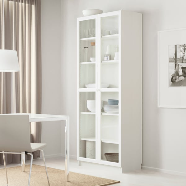 White BILLY bookcase with glass doors, tall, near table and chairs.