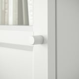 A white BILLY bookcase door hinge, round, on a white wooden door.