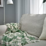 BISKOPSMÖSSA throw on sofa, green pattern, soft, fringed, covers pillow, near lamp.
