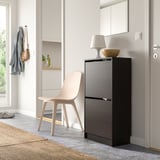 Minimalist entryway with black shoe cabinet, chair, mirror, lamp, bowl, coat.