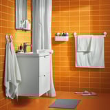Bright bathroom with orange tiles, white sink vanity, white towels, and a white shower curtain with a shelf holding toiletries.