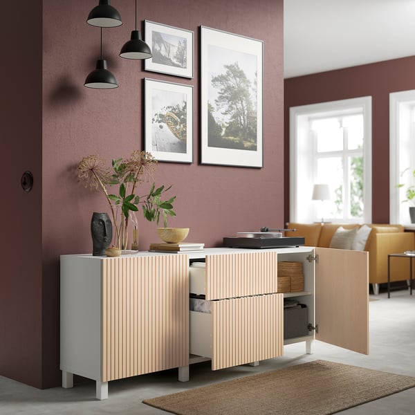 Modern cabinet with open door, displaying interior storage. Decorative items on top, set against burgundy wall with art.