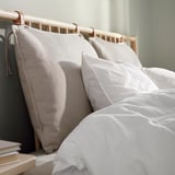 This image shows a modern, light-colored wooden bed with white pillows and a gray bedspread. The bed frame has a sleek, minimalist design.