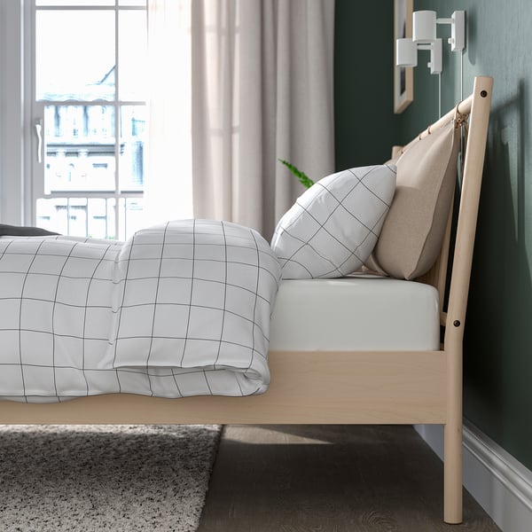 Cozy bed with grid bedding and beige headboard, showcasing adjustable slats for mattress support and air circulation, positioned near a window.