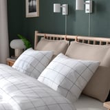 Cozy bedroom with grid-patterned bedding, beige pillows, wood headboard, wall lamps, and nightstand with a lamp.