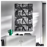 Large black and white cityscape art in a white frame hangs above a white locker cabinet. Green cactus decoration, books, and a camera on the cabinet.