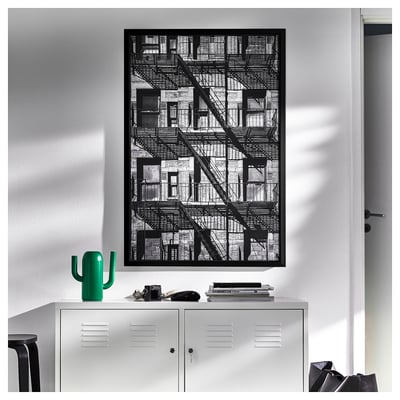Large black and white framed art of building with stairs. White wall, grey locker, green cactus decor.