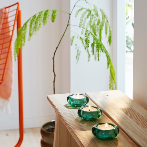 Three tealight holders on wooden shelf, lit, with fern plant.