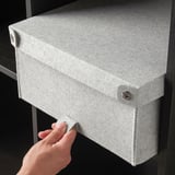 Image description: hand opening a grey felt storage box, likely BLÄDDRA, designed to hide items neatly. Fits into kallax shelving.