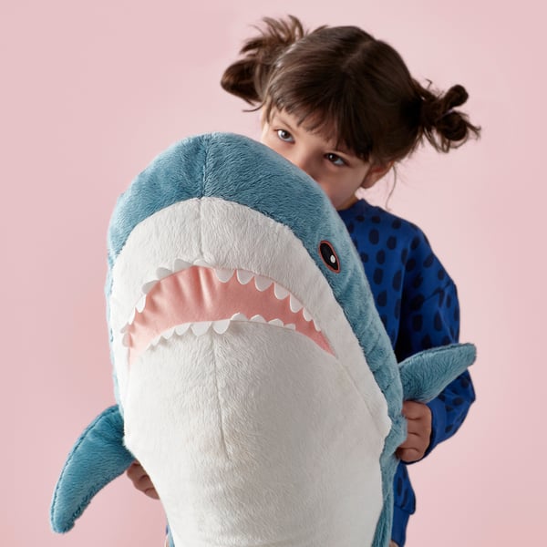 Little girl hugs large soft shark plush toy. Blue & white, ce marked, ages 18+ months.