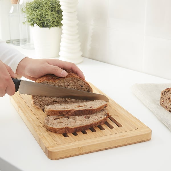 Person slicing bread on a wooden cutting board designed with grooves to collect crumbs.
