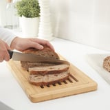 Person slicing bread on a wooden cutting board designed with grooves to collect crumbs.